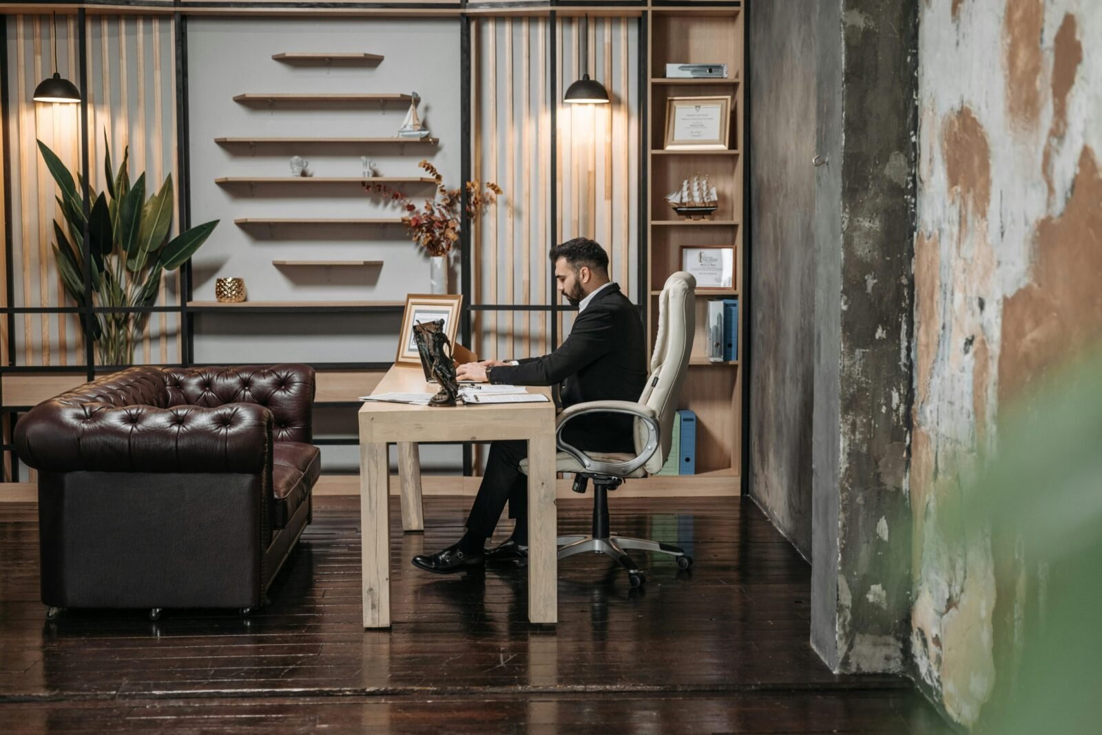 A man in a suit working at a desk in a stylishly designed office with wooden shelves.